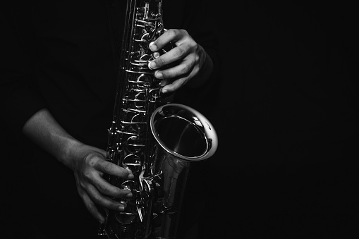 close up of Young Saxophone Player hands  playing alto sax musical instrument over a black  background,  closeup with copy space, vintage tone,  can be used for music background