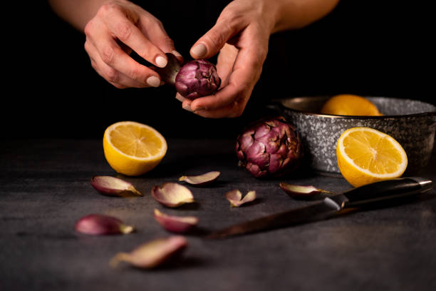 Close up on hands cleaning ripe artichoke on black table. stock photo