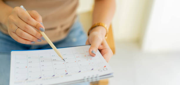 close up on senior employee woman hand using pen to writing schedule on calendar to make appointment meeting or manage timetable each day at house for work from home concept - data imagens e fotografias de stock