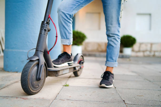 close-up op vrouw benen voeten staande op de elektrische kick scooter op de stoep dragen jeans en sneakers in de zomerdag - elektrische step stockfoto's en -beelden