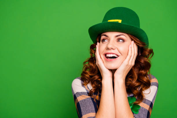 Close up photo of she her curly brunette arms on cheekbones looking to empty space admiring wear casual checkered plaid shirt leprechaun headwear isolated green vivid bright vibrant background Close up photo of she her curly brunette arms on cheekbones looking to empty space admiring wear casual checkered plaid shirt leprechaun headwear isolated green vivid bright vibrant background irish women stock pictures, royalty-free photos & images