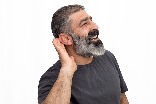 Close up portrait of curious interested delightful funny amazed cheerful surprised mature man holding hand near ear and trying to hear the information isolated on white.