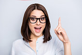 istock Close up portrait of pretty, charming, glad woman in shirt, eyewear finding an idea, resolution, showing index finger up with open mouth, isolated on grey background 956564854