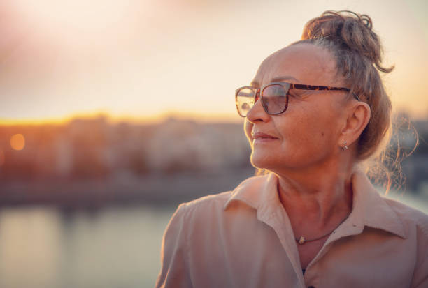 Close up portrait of stylish beautiful mature senior woman wearing glasses 60 years old looking to the side in sunset light stock photo