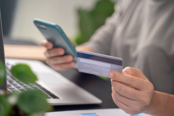 Close up shot of females hands holding credit card typing message on smart phone for shopping online stock photo