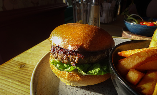 Plain hamburger on plate served with bowl of chips in lunchtime sunshine