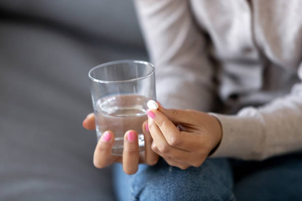 close-up zieke vrouw holding glas met water en pil in handen - pijnstiller stockfoto's en -beelden
