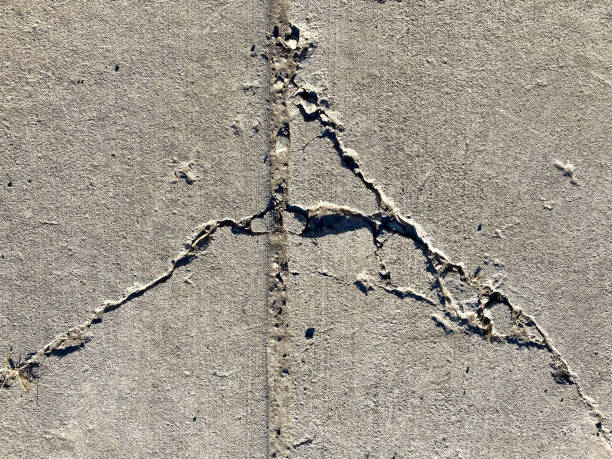 close up view of concrete sidewalk cracks damage in natural sunlight showing deep shadows stock photo
