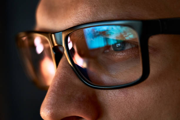Close up view of focused businessman wears computer glasses for reducing eye strain blurred vision looking at pc screen with computer reflection using internet, reading, watching, working online late. Close up view of focused businessman wears computer glasses for reducing eye strain blurred vision looking at pc screen with computer reflection using internet, reading, watching, working online late. image focus technique stock pictures, royalty-free photos & images