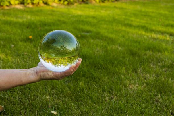 Close up view of hand holding crystal ball with inverted image of green natural landscape. Close up view of hand holding crystal ball with inverted image of green natural landscape. reentry stock pictures, royalty-free photos & images
