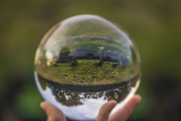 Close up view of hand holding crystal ball with inverted image of green natural landscape. Close up view of hand holding crystal ball with inverted image of green natural landscape. reentry stock pictures, royalty-free photos & images
