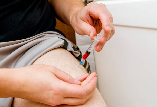 Close up view of man person do the B12 vitamin injection shot in home itself to himself in leg( vastus lateralis muscle) due to B12 deficiency what body do not absorb orally and do not produce. stock photo