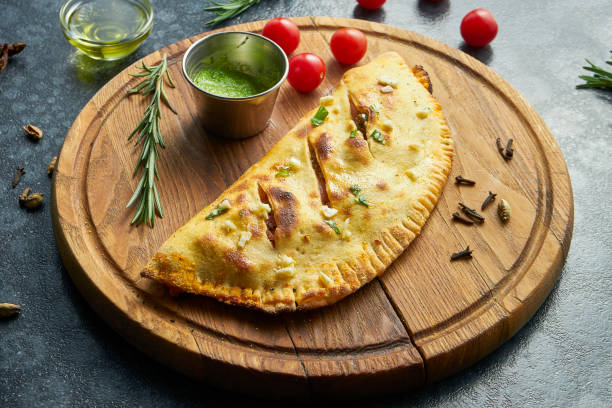 Close up view on Homemade and lush calzone pizza with meat on a wooden tray and sauce on a dark background. Tasty food for lunch. Flat lay stock photo