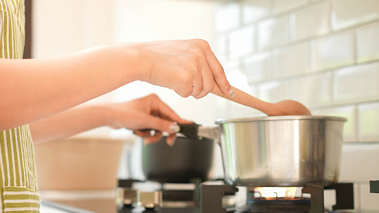 close up woman hand use spatula to stirring soup in the pot in kitchen room to make lunch or dinner for routine lifestyle and health food concept
