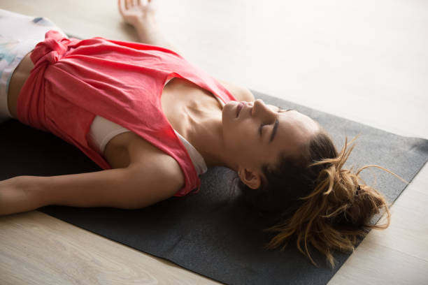 Close up woman in shavasana or dead body position. Close up image of young active woman lying on yoga mat in shavasana posture, dead body pose, resting after yoga class at home or in studio, relaxing, breathing, deep meditation, refreshment moment. lying down stock pictures, royalty-free photos & images