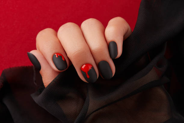 Close up womans hand with halloween manicure on red background holding fabric. Manicure, pedicure beauty salon concept stock photo