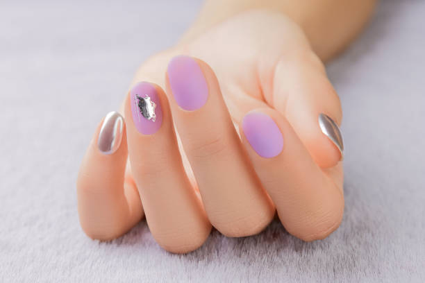 Close up womans hand with matte lavender nail design on gray furry background stock photo