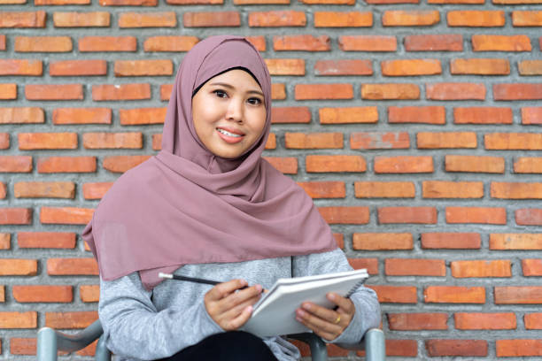 close up young beautiful teacher muslim woman sitting at brick wall school building background and smiling with using pencil for writing on book , education lifestyle people concept close up young beautiful teacher muslim woman sitting at brick wall school building background and smiling with using pencil for writing on book , education lifestyle people concept indonesian girl stock pictures, royalty-free photos & images