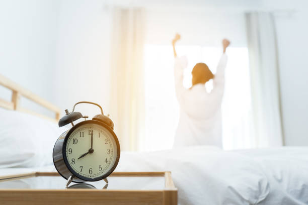 Closeup alarm clock, Young asian woman wake up in the moring and stiing on bed at mirror door side relaxing in holiday with sunlight  waking up stock pictures, royalty-free photos & images