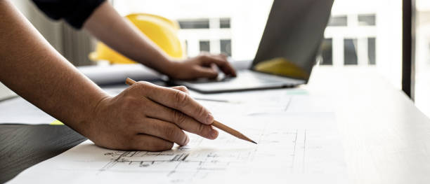 A close-up, an architect, a house designer holding a pencil, pointing to a house plan to examine the design plan before discussing the details with the client. Interior design and decoration ideas. stock photo