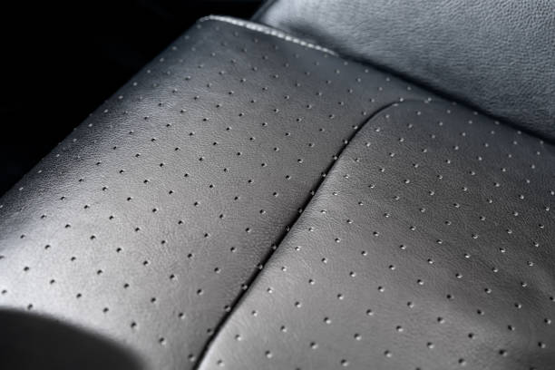 Close-up detail view of modern black perforated dotted ventilated luxury car seat. Part of dark vehicle interior. Auto detailing and leather polish skin cleaning wash and care concept stock photo