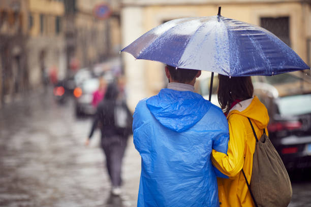 Close-up from back of a young couple in love who is walking the city on a rainy day. Walk, rain, city, relationship stock photo