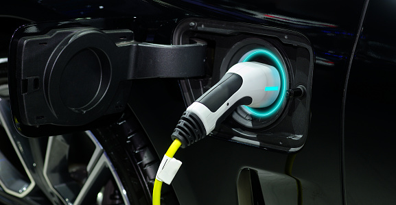 Close-up hand grip plug of industrial electric charging machine connected with socket  charge on black modern car for rechargeable battery, zero emission vehicle (ZEV) and green energy for smart life