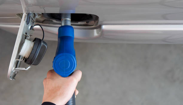 Closeup hand holding blue gas pump nozzle. Gas station worker filling up bronze pickup truck tank (Top View). stock photo