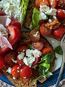 Stock photo showing elevated view of plate of bruschetta open sandwich with crusty, toasted slices of wholemeal bread, garlic and pesto sauce with red cherry tomatoes, sliced red onion and crumbled feta cheese on a blue rimmed plate, healthy eating.