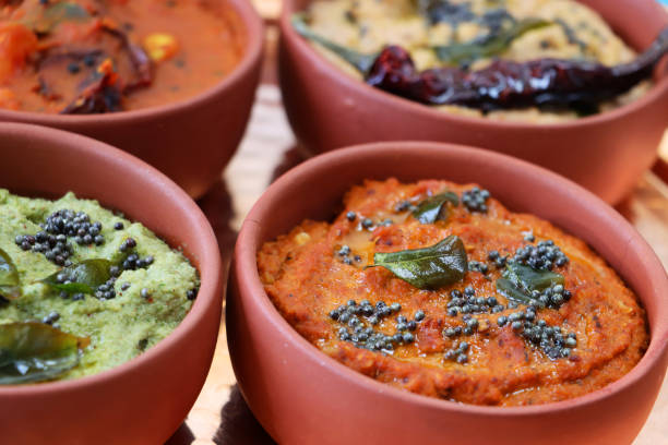 Close-up image of orange, terracotta pots of Indian savoury dips, bowls of coconut chutney, mint and coriander chutney, ginger, chilli and garlic dip, and peanut chutney, elevated view, focus on foreground Stock photo showing close-up, elevated view of Indian savoury dips served in orange, terracotta pots. Dishes of tasty sambar, coconut chutney, mint and coriander chutney, ginger, chilli and garlic dip, and peanut chutney, popular in India / Pakistan. chutney stock pictures, royalty-free photos & images