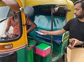 istock Close-up image of passenger paying tuk tuk driver at journey's end, green and yellow auto rickshaw parked at roadside curb being paid fare, focus on foreground 1410957708