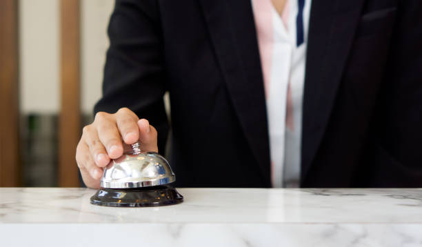 Closeup of a businesswoman hand ringing silver service bell on hotel reception desk. stock photo