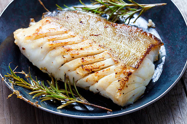 Close-up of a cod fillet with rosemary on a plate Fried fish fillet, Atlantic cod with rosemary in pan cod stock pictures, royalty-free photos & images