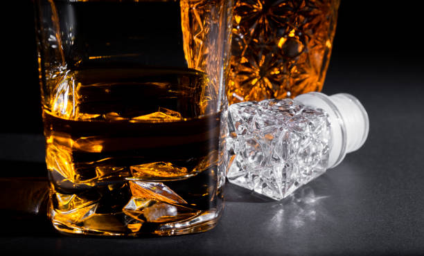 Close-up of a crystal glass along with a bottle full of whiskey on black background. Coktails and spirits stock photo