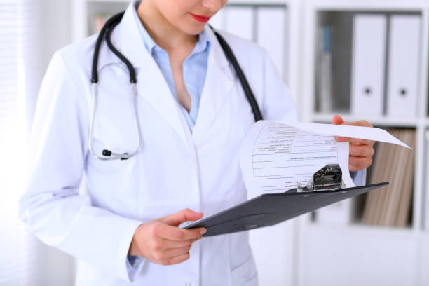 Close-up of a female doctor is filling out application form or...