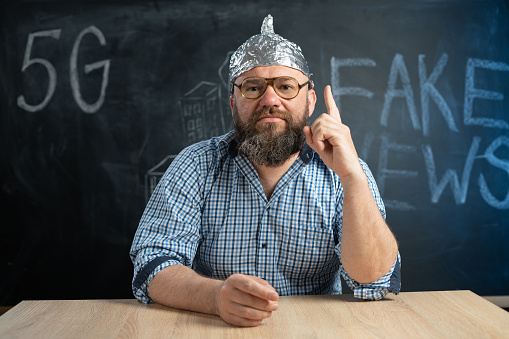close-up of a male conspiracy theorist in a protective foil cap and glasses debunks myths. Conspiracy theory and the harm of the 5g network. Mobile killer. The schizophrenic works. Copy space.