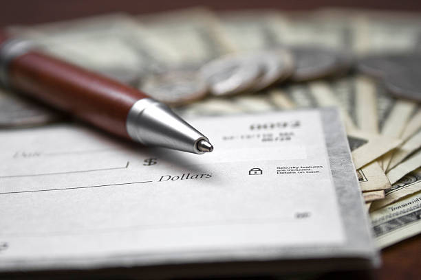 Close-up of a pen and check book on top of dollar bills stock photo