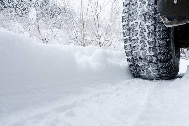 Close-up of a rear black tire in the snow creating tracks stock photo