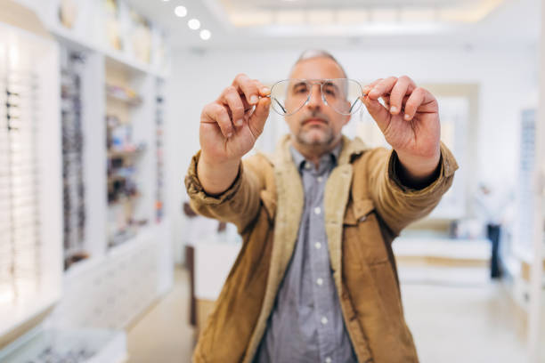 Close-up of a serious mature man holding modern eyeglasses in his hands, in an optician's shop. stock photo
