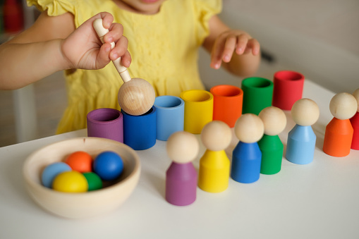 Close-up of a sorter toy with balls, cups and a wooden spoon. The child plays and educational games to learn shapes and colors. Figurines in the form of little men. A girl plays in the children's room