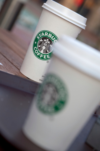 izmir, Turkiye - June 1, 2011: two starbucks coffee cup on the wooden table. Starbucks is the world\'s largest coffeehouse company. The cup in the center shows the old version of the logo.