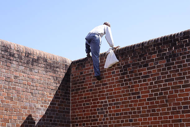 Close-up of a thief climbing over a brick wall up and over, doing a runner, actually a mannequin made to look bad.  escaping stock pictures, royalty-free photos & images