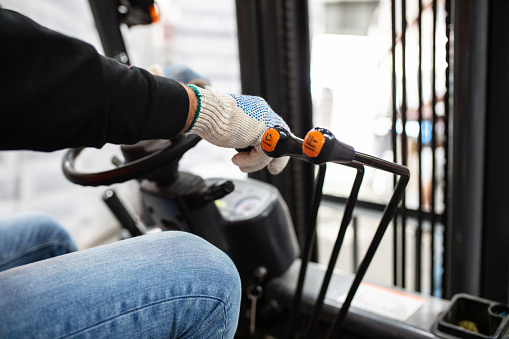 Close-up of a warehouse worker driving forklift. Worker hands operating forklift in distribution warehouse.