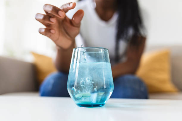 Closeup of a young woman dropping an effervescent antacid in a glass of water. young woman hardly put a soluble pill with a medicine for pain or a hangover in a glass of water Closeup of a young woman dropping an effervescent antacid in a glass of water. young woman hardly put a soluble pill with a medicine for pain or a hangover in a glass of water sparkling water stock pictures, royalty-free photos & images