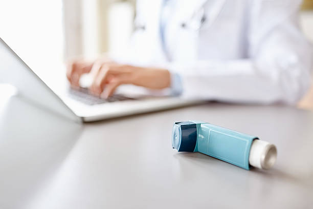Close-up of asthma inhaler with doctor using laptop at desk stock photo