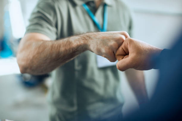 Close-up of auto repairmen greeting with fists at car workshop. stock photo
