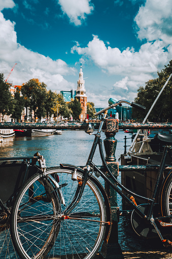 Close-up of Bike parked on a bridge in Amsterdam, Netherlands. Typical cityscape with Amstel river and motion clouds at the background.