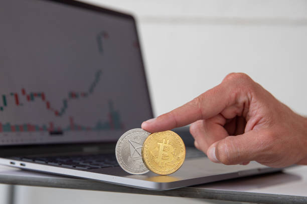 Close-up of Bitcoin and Ethereum cryptocurrencies held up by a finger with candlestick charts in the background of a laptop. Trading of cryptos, new virtual money. Crypto currency. Close-up of Bitcoin and Ethereum cryptocurrencies held up by a finger with candlestick charts in the background of a laptop. Trading of cryptos, new virtual money. Crypto currency.  With Ethereum  stock pictures, royalty-free photos & images