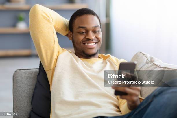 Closeup of black guy sitting on couch, using smartphone