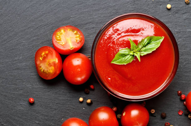 Close-up of bowl of homemade ketchup made from fresh cherry tomatoes, garlic, basil on black slate plate. Top view. stock photo